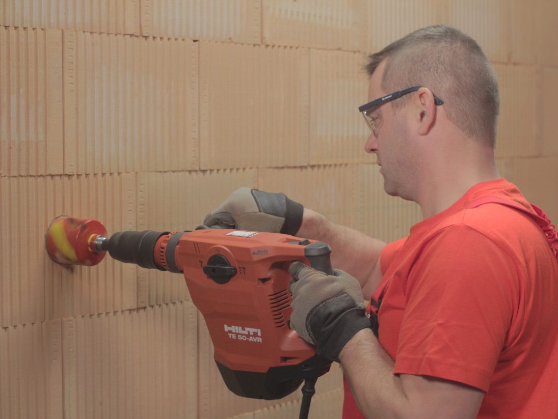 A man drilling holes for electrical boxes into a brick wall