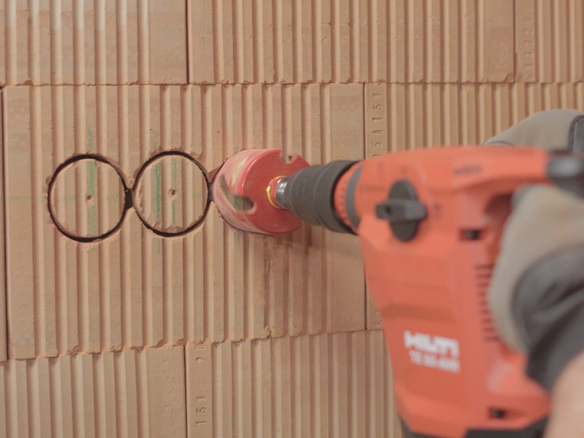 Male hands holding drill and cutting a holes for electrical boxes in a brick wall