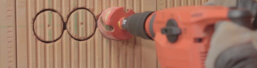 Male hands holding drill and cutting a holes for electrical boxes in a brick wall