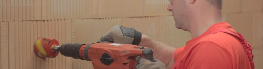 A man drilling holes for electrical boxes into a brick wall