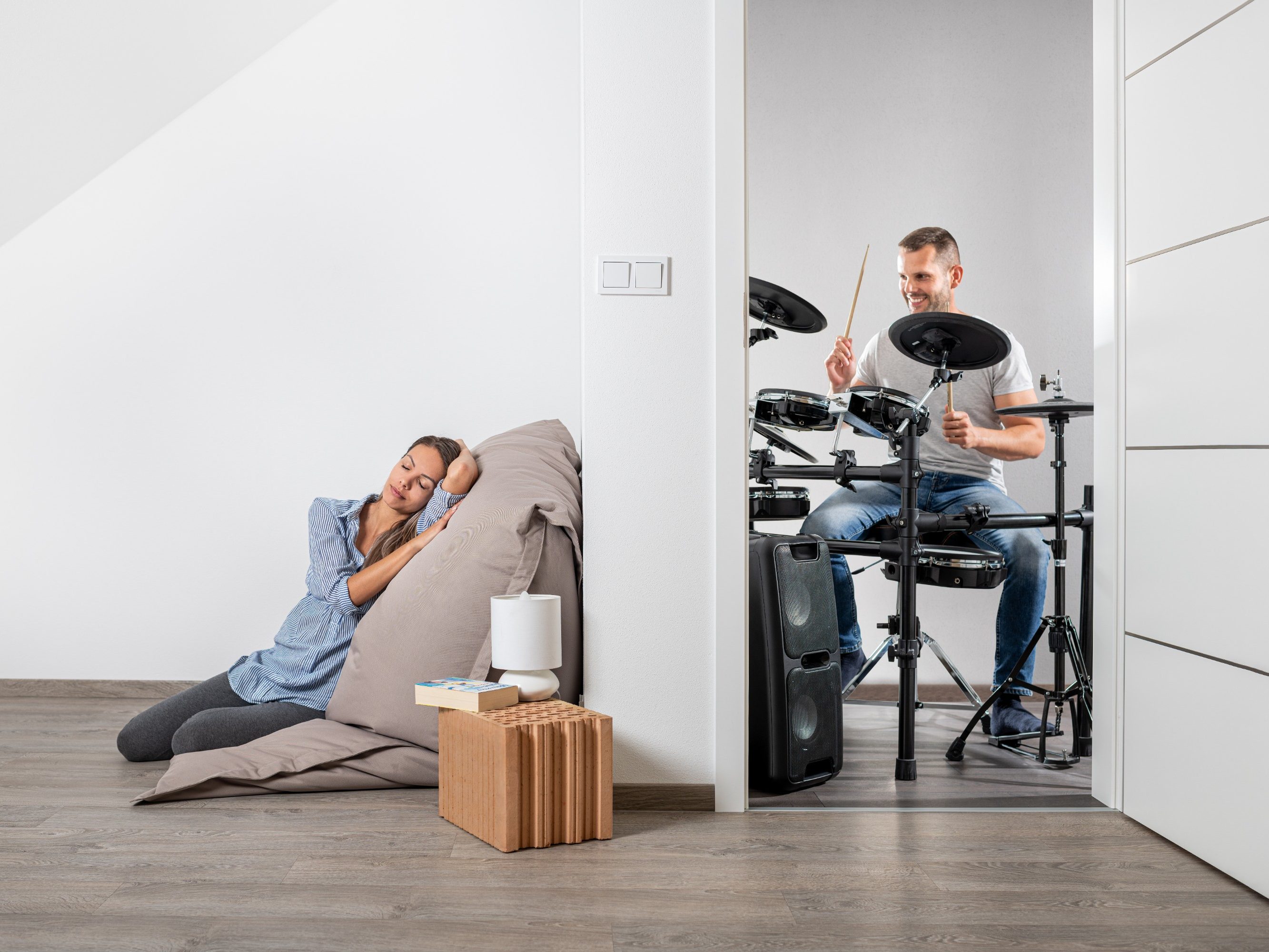 Muž hrající na bicí a v druhé místnosti klidně ležící žena cz
