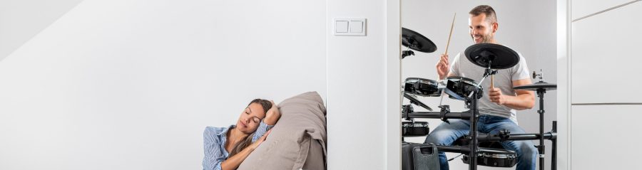 Muž hrající na bicí a v druhé místnosti klidně ležící žena cz