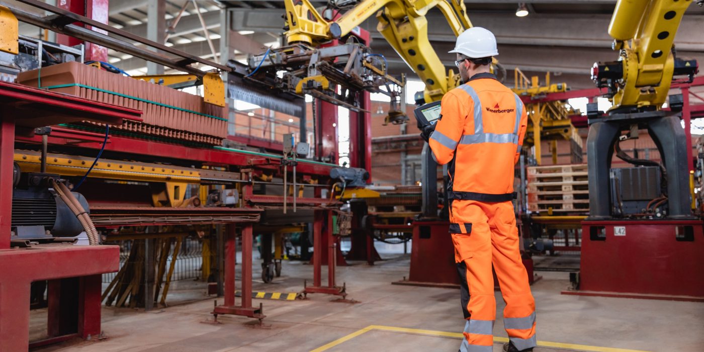 Muž v pracovním oblečení a helmě stojící ve výrobním závodě